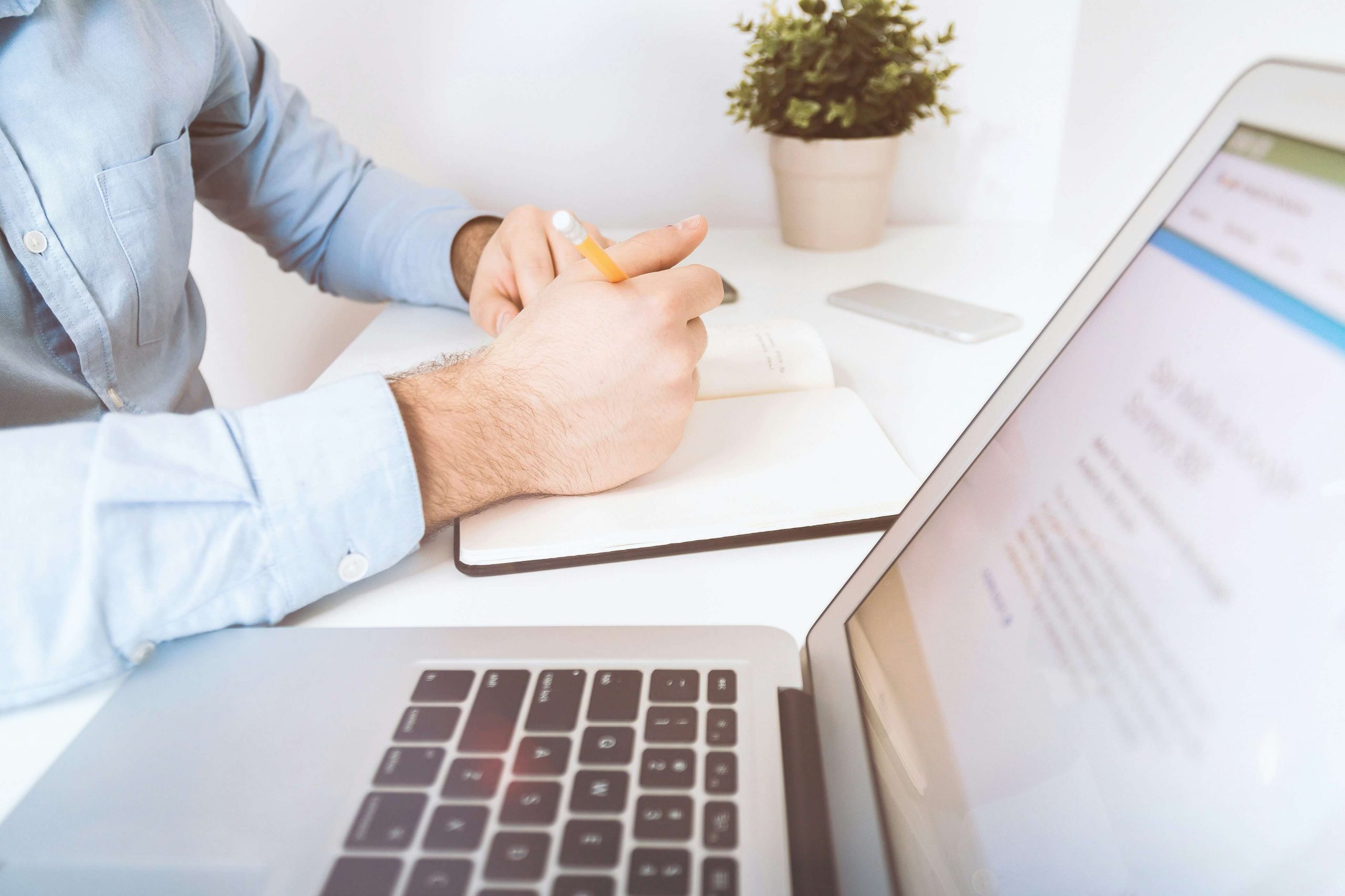Man writing notes at desk with laptop